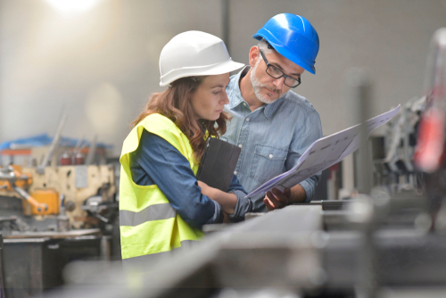 Two engineers in hard hats reviewing plans on site